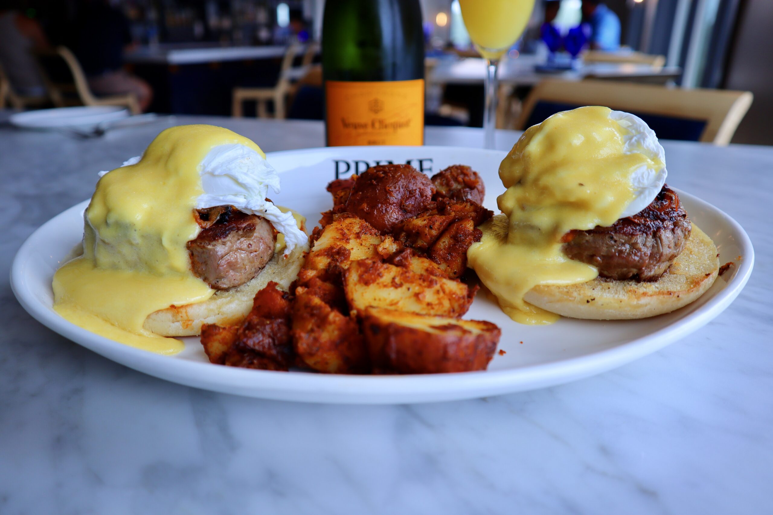 Two eggs Benedict with poached eggs and hollandaise sauce, served with seasoned potatoes and champagne.